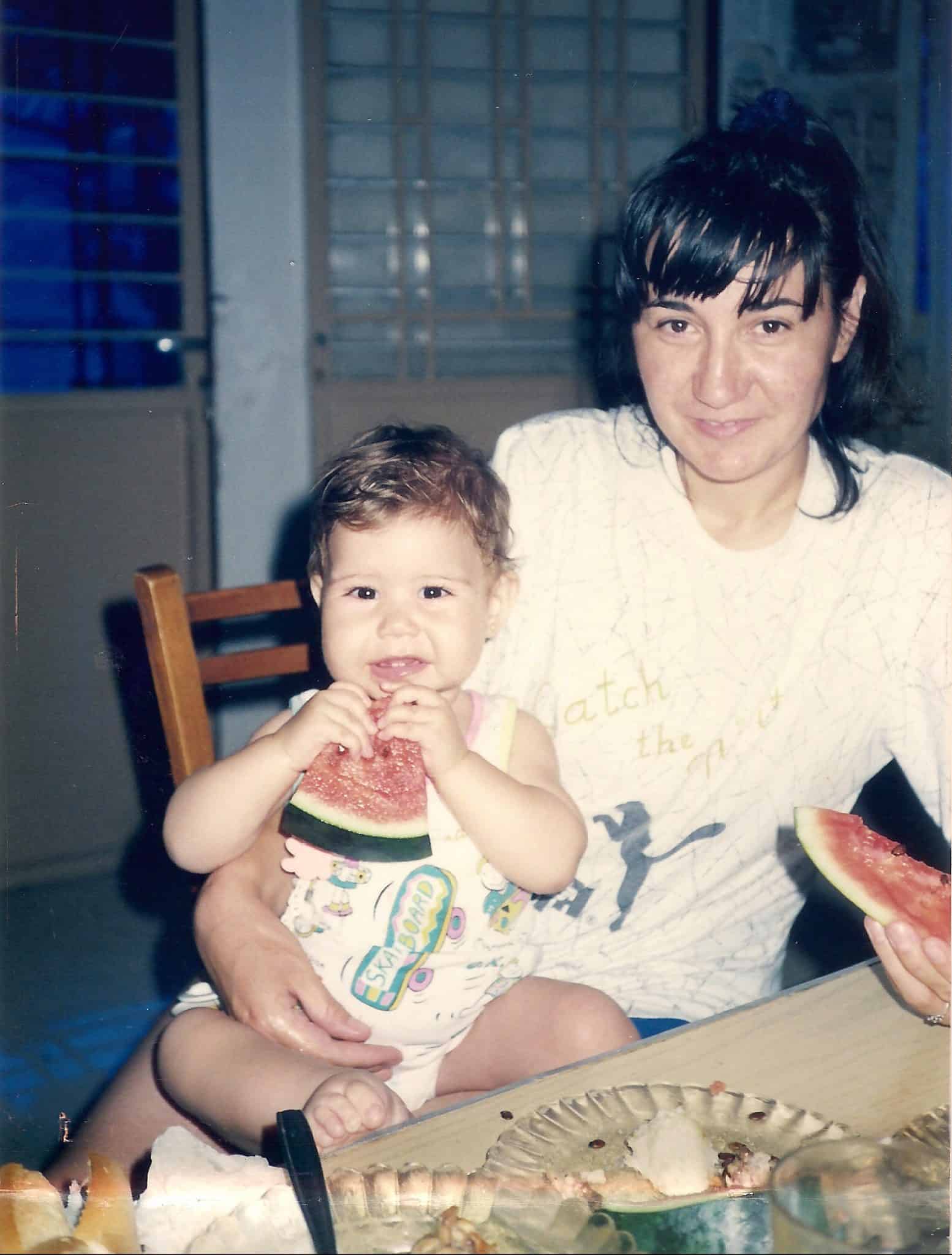 Woman holding a toddler while both eat watermelon.