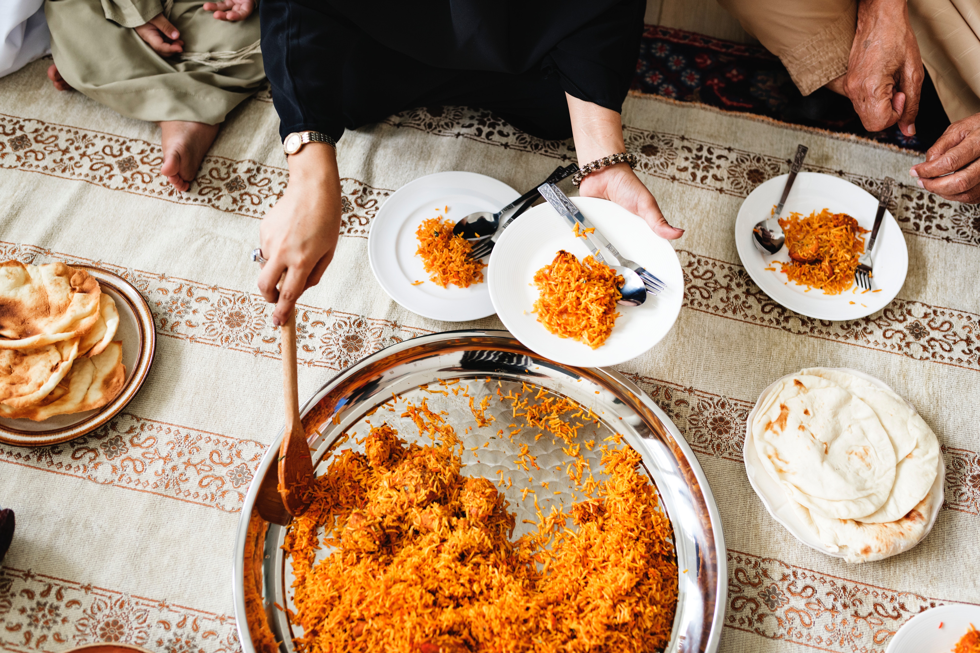 Woman serving rice onto a plate while sitting on a blanket on the floor.