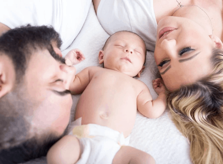 mom and dad laying with baby on a white bed